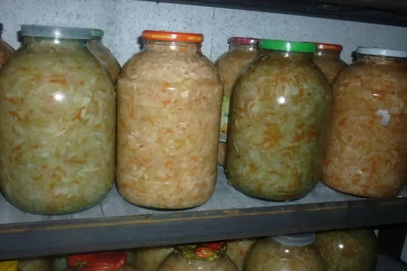Банки с квашеной капустой на полках в погребе